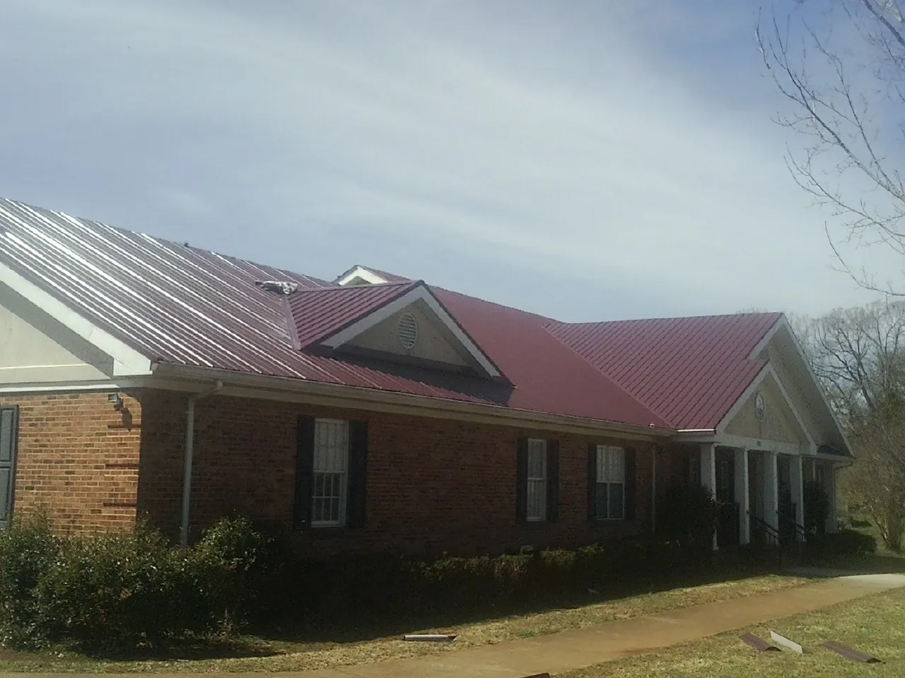 Red metal roof with gabled entries on a long brick building, from a Hail Damage Roof Repair job in Thompsons