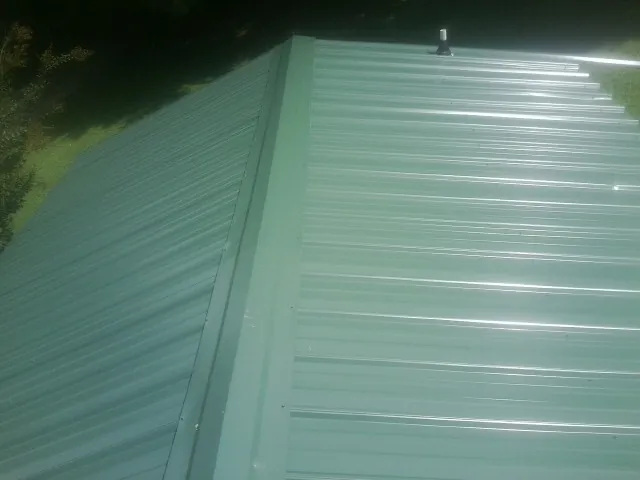 New green metal panels meeting at the ridge of a roof — Flat Roof Repair work by our crew in Thompsons