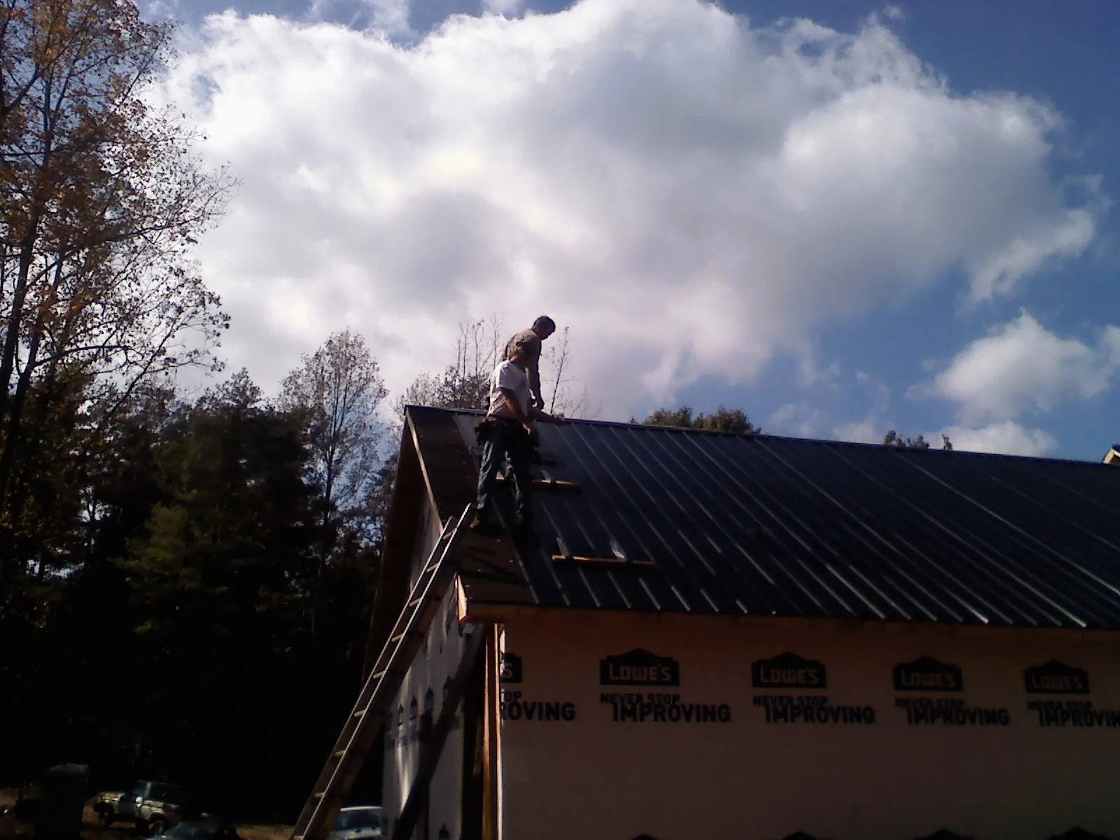 Roofer fastening dark metal panels high against a cloudy sky in Thompsons