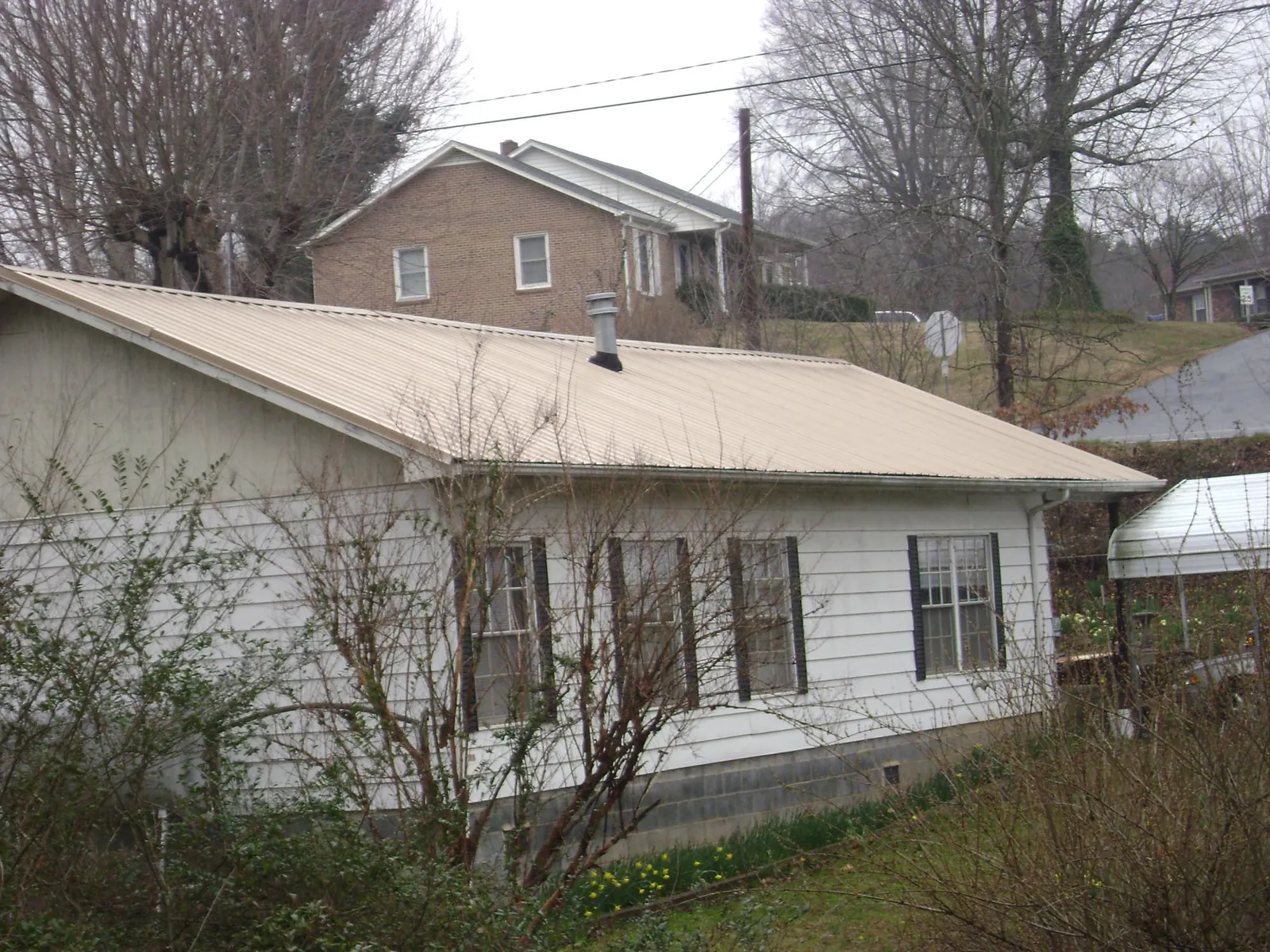 Tan metal roof on a white sided house set into a hillside — Commercial Roofing by Roofing Brothers in Thompsons